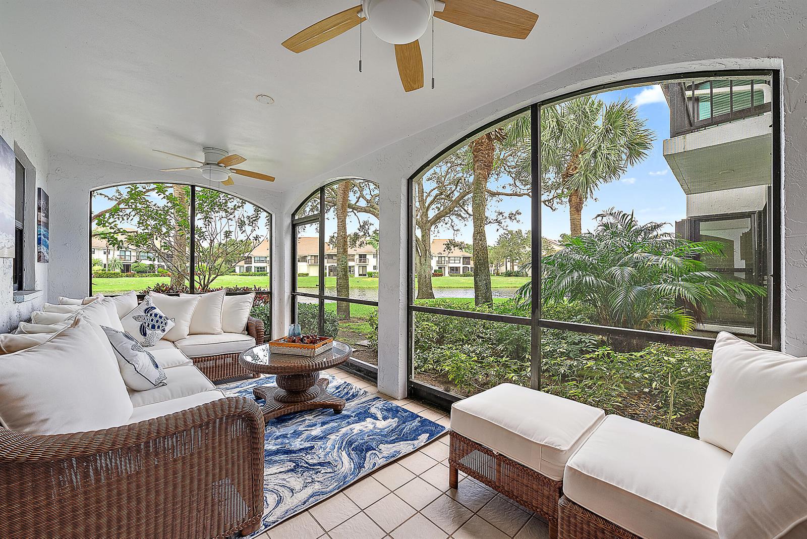 A screened-in patio features wicker furniture, a blue patterned rug, and views of a pond — 16695 Traders Crossing N # 118, Jupiter FL 33477, JUPITER, FL