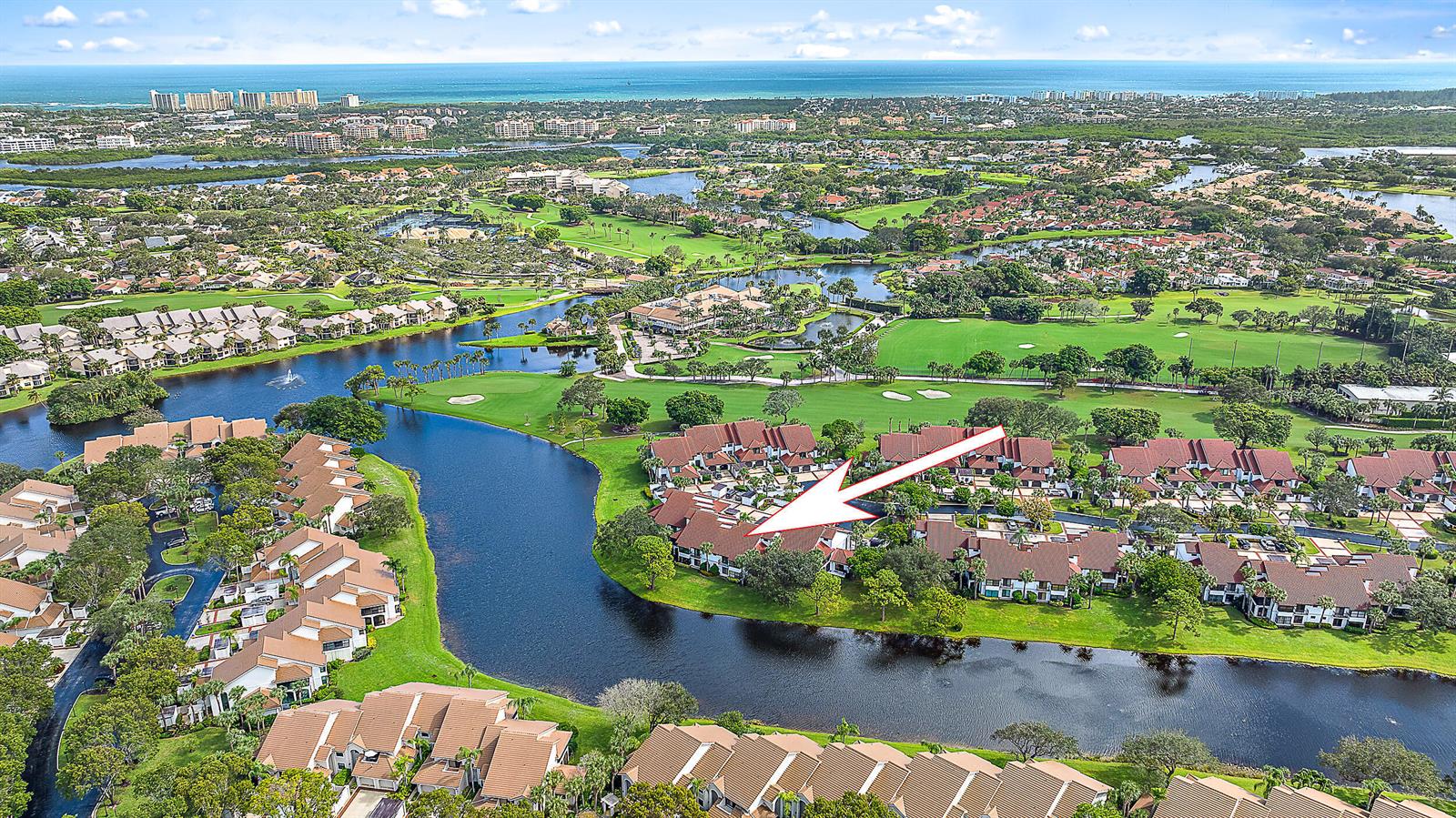 An aerial view shows a residential complex with brown roofs situated along a winding canal — 16695 Traders Crossing N # 118, Jupiter FL 33477, JUPITER, FL