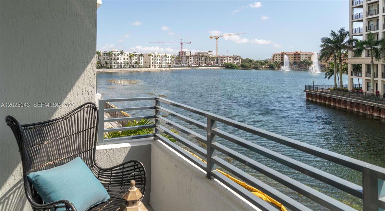 A balcony with a black wicker chair overlooks a lake with fountains and construction cranes — 4720 NW 85th Ave # A2, Doral FL 33166, DORAL, FL