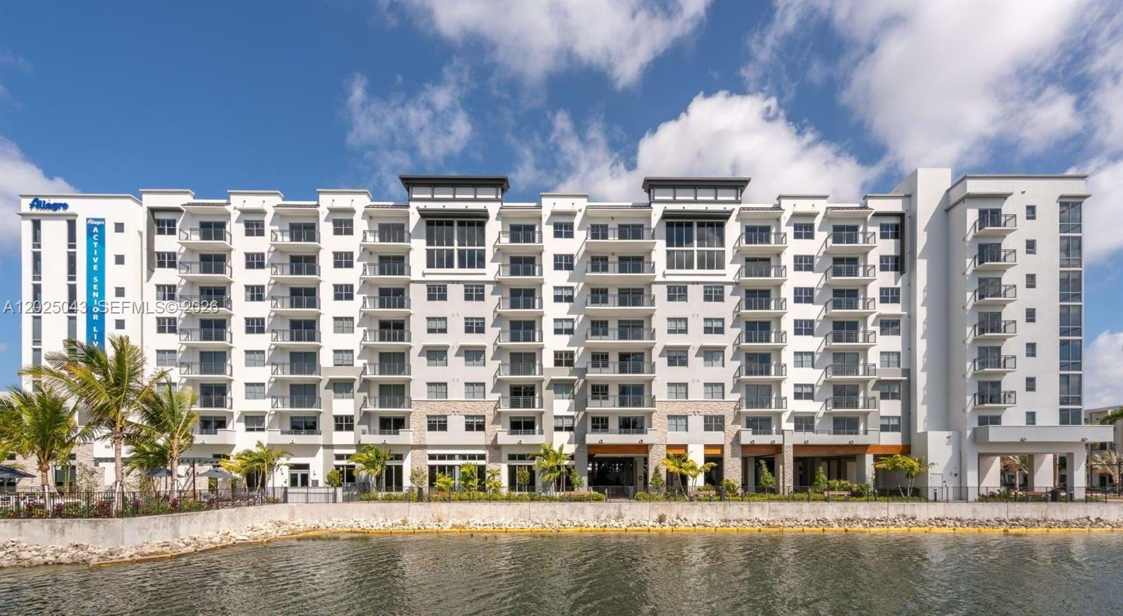 A multi-story apartment building with balconies stands along the edge of a calm lake — 4720 NW 85th Ave # A2, Doral FL 33166, DORAL, FL