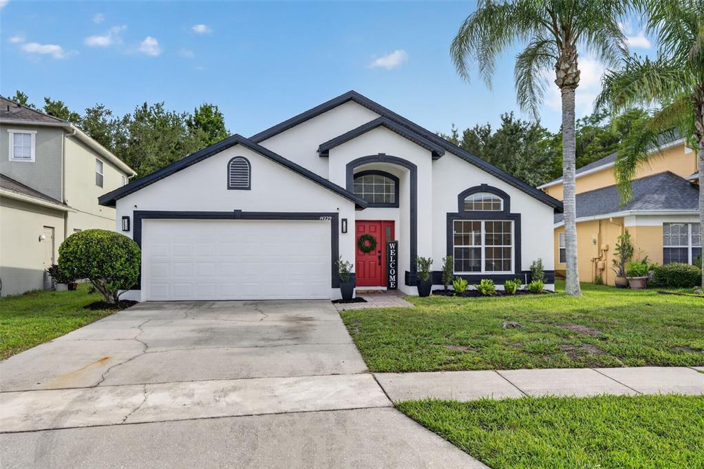 A single-story house with a white stucco exterior, dark trim, a red door, and garage — 14229 SAPPHIRE BAY CIRCLE, ORLANDO, FL