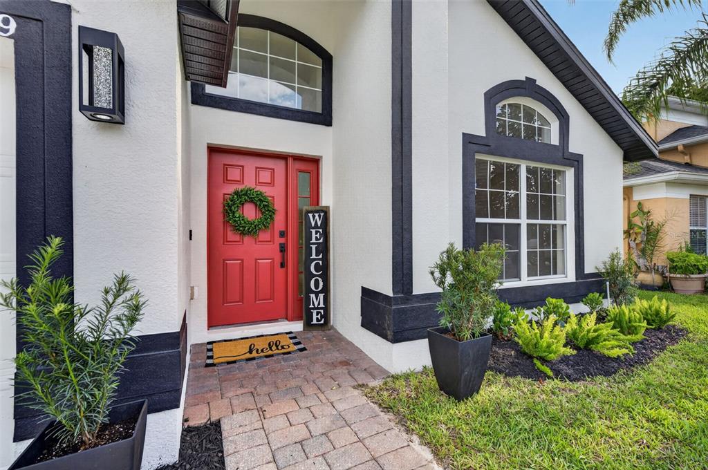The exterior of a house features a red front door, a welcome sign, and landscaping — 14229 SAPPHIRE BAY CIRCLE, ORLANDO, FL