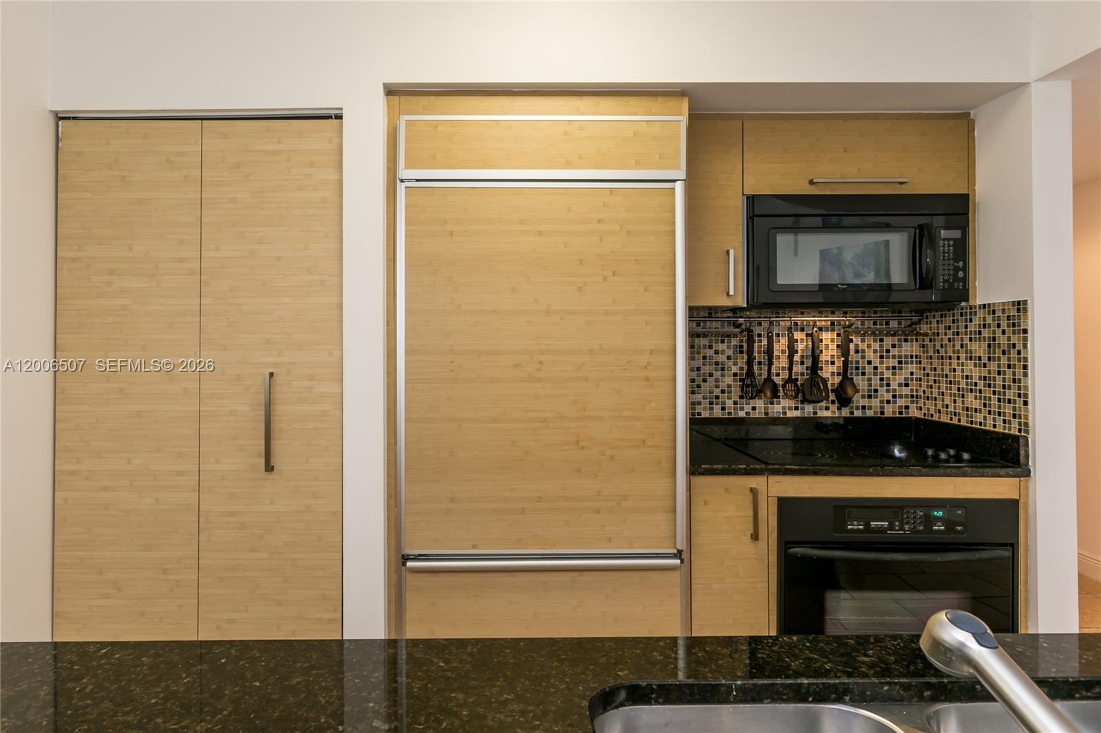 A kitchen features bamboo-paneled cabinetry, a built-in refrigerator, black appliances, and dark granite countertops — 1830 S OCEAN DR # 4010, Hallandale Beach FL 33009, HALLANDALE BEACH, FL