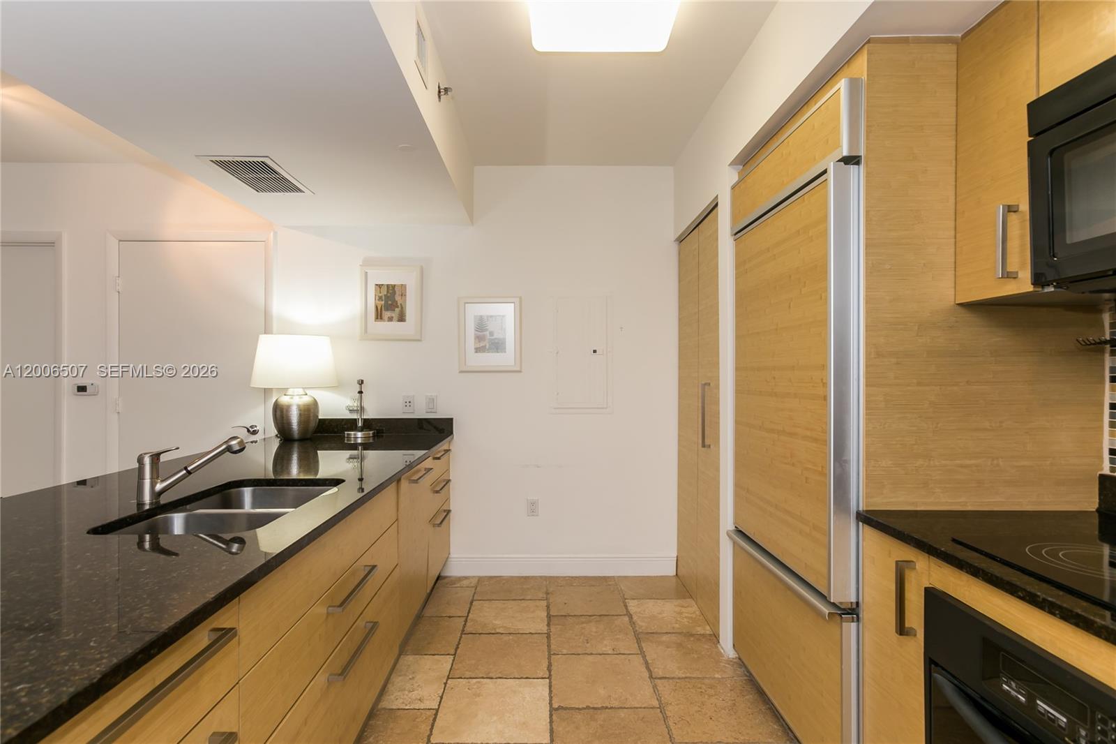A kitchen features light wood cabinetry, black granite countertops, and stone tile flooring — 1830 S OCEAN DR # 4010, Hallandale Beach FL 33009, HALLANDALE BEACH, FL