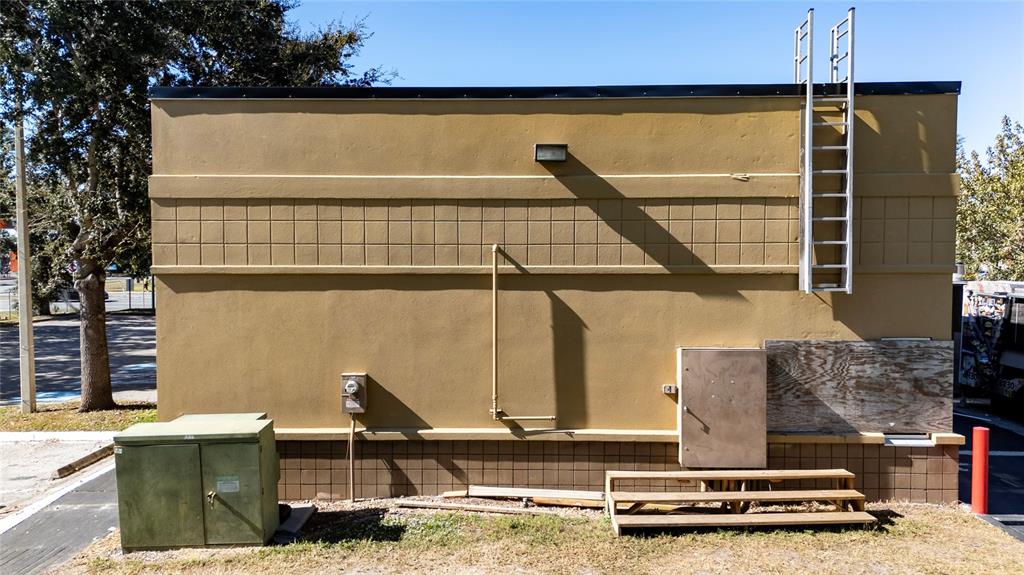 The exterior of a tan commercial building features a metal ladder, utility boxes, and steps — 7155 S ORANGE BLOSSOM TRAIL, ORLANDO, FL