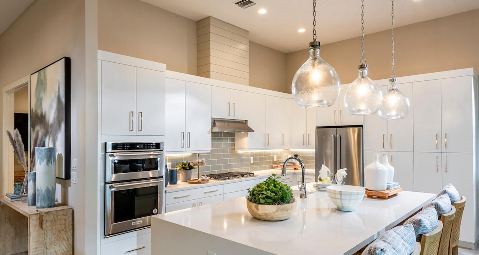 A modern kitchen features white cabinetry, a large island, stainless steel appliances, and glass pendant lights — 9858 Regency Way, Palm Beach Gardens FL 33412, PALM BEACH GARDENS, FL
