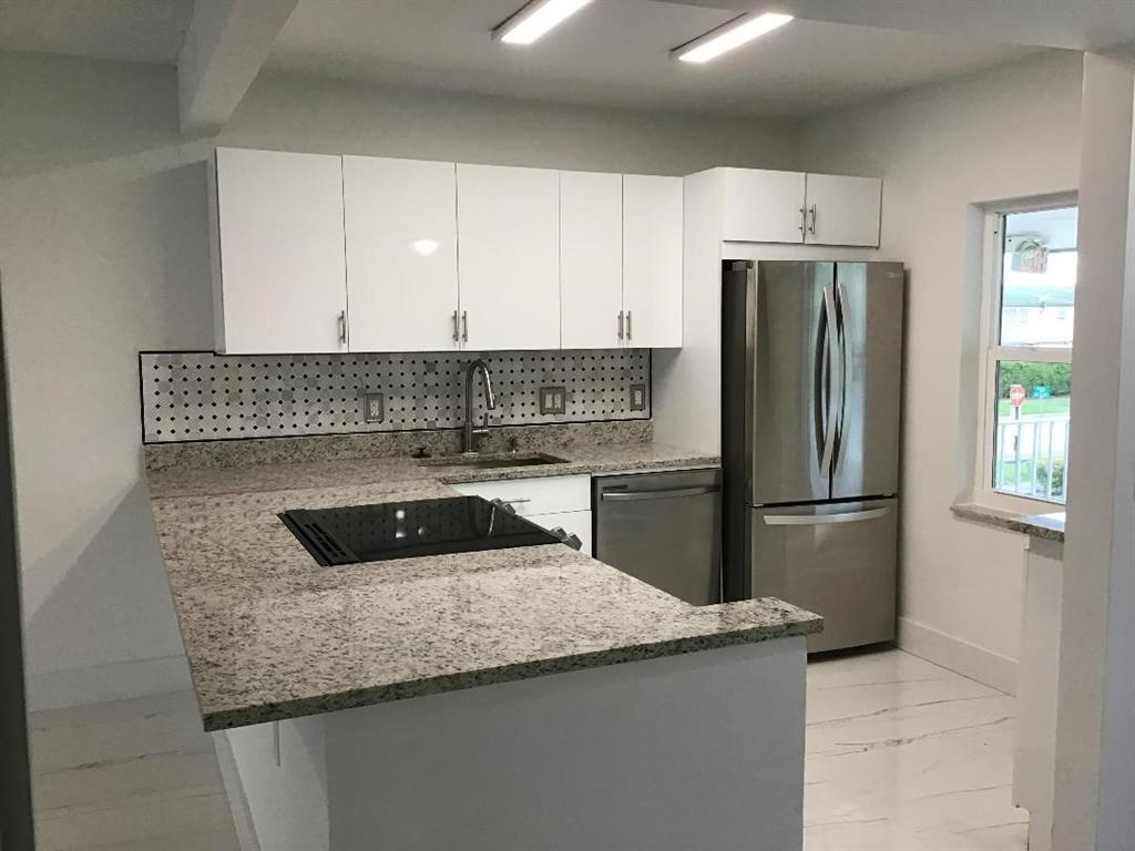 A kitchen features white cabinets, granite countertops, a stainless steel refrigerator, and a pegboard backsplash — 7600 NW 4th Place # 207, Margate FL 33063, MARGATE, FL