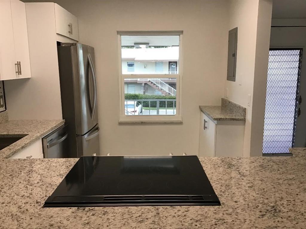 A kitchen features white cabinets, granite countertops, a stainless steel refrigerator, and a window view — 7600 NW 4th Place # 207, Margate FL 33063, MARGATE, FL