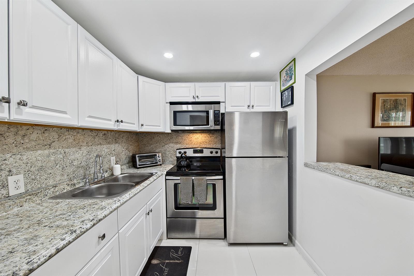 A kitchen features white cabinets, granite countertops, stainless steel appliances, and a pass-through window — 96 Fanshaw C, Boca Raton FL 33434, BOCA RATON, FL
