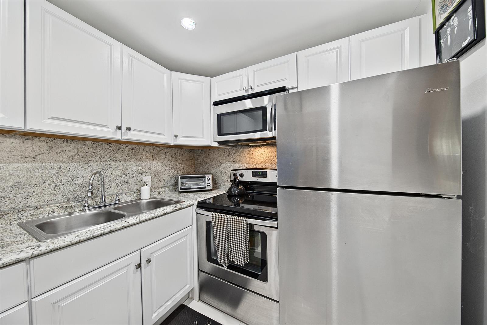 A kitchen features white cabinets, stainless steel appliances, and speckled granite countertops — 96 Fanshaw C, Boca Raton FL 33434, BOCA RATON, FL