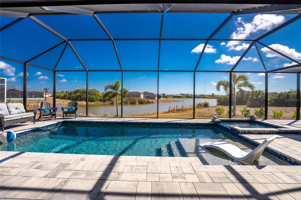 A screened-in pool patio overlooks a lake with lounge chairs and a spa — 401 ALBATROSS ROAD, ROTONDA WEST, FL