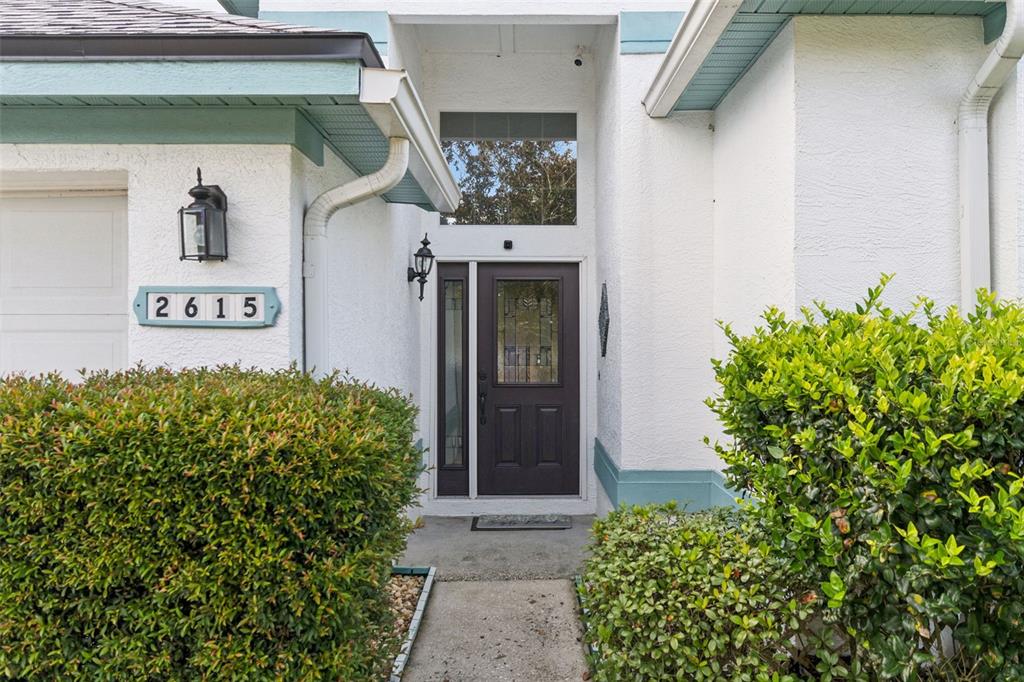 The exterior of a house features a dark front door, white stucco walls, and landscaping — 2615 BURWOOD AVENUE, ORLANDO, FL