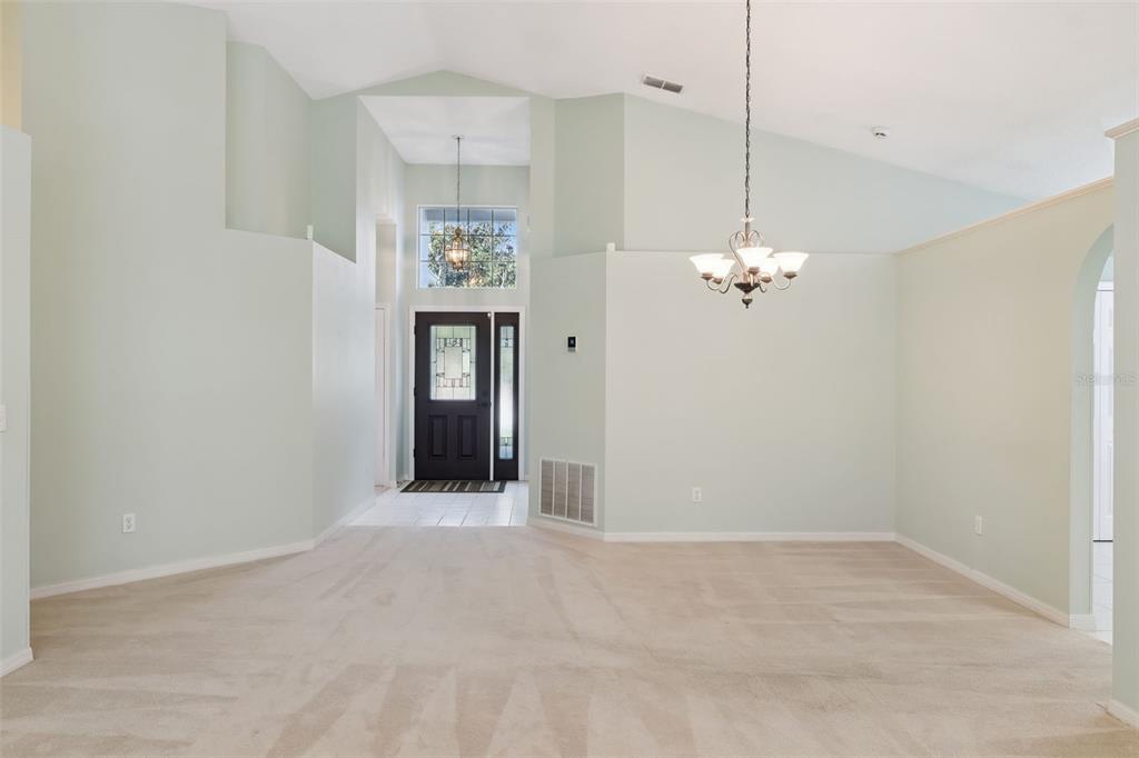 A spacious living area with vaulted ceilings, beige carpeting, and a dark front door — 2615 BURWOOD AVENUE, ORLANDO, FL