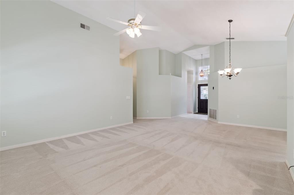 An empty room with light green walls, beige carpeting, a ceiling fan, and a chandelier — 2615 BURWOOD AVENUE, ORLANDO, FL