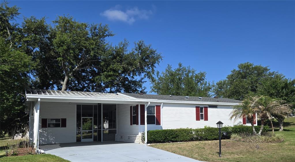 A white single-story manufactured home features a metal carport, red shutters, and a grassy yard — 4122 MYRTLE OAK COURT UNIT 851, ZELLWOOD, FL
