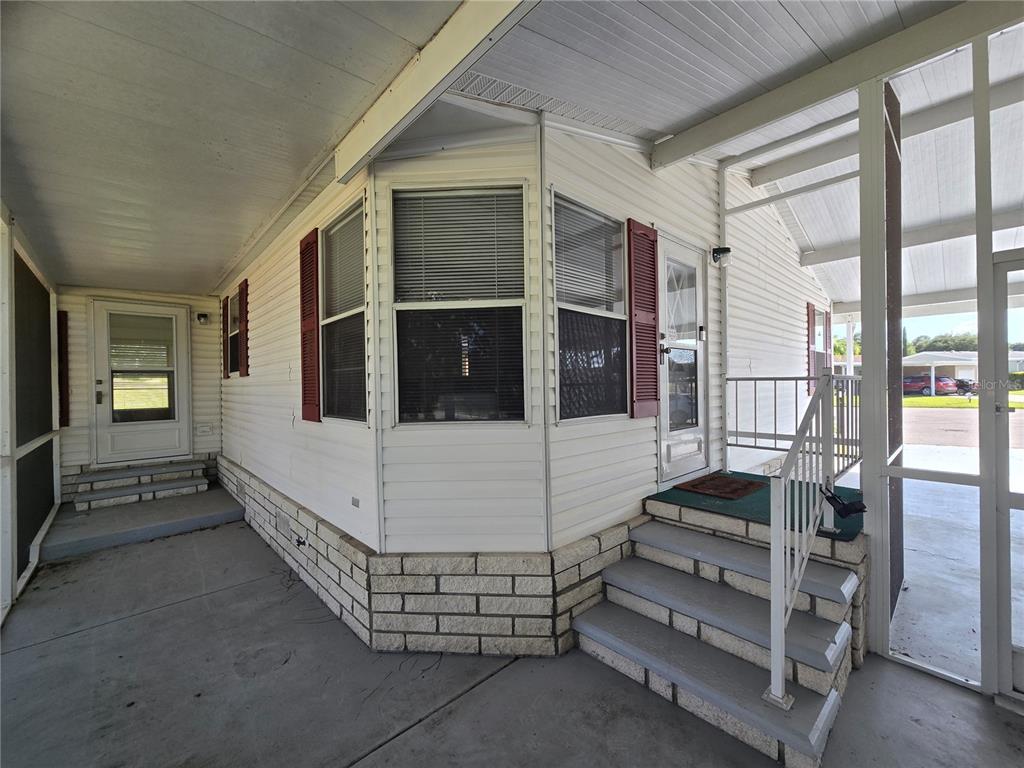 A white mobile home exterior features a concrete patio, stairs, and red window shutters — 4122 MYRTLE OAK COURT UNIT 851, ZELLWOOD, FL