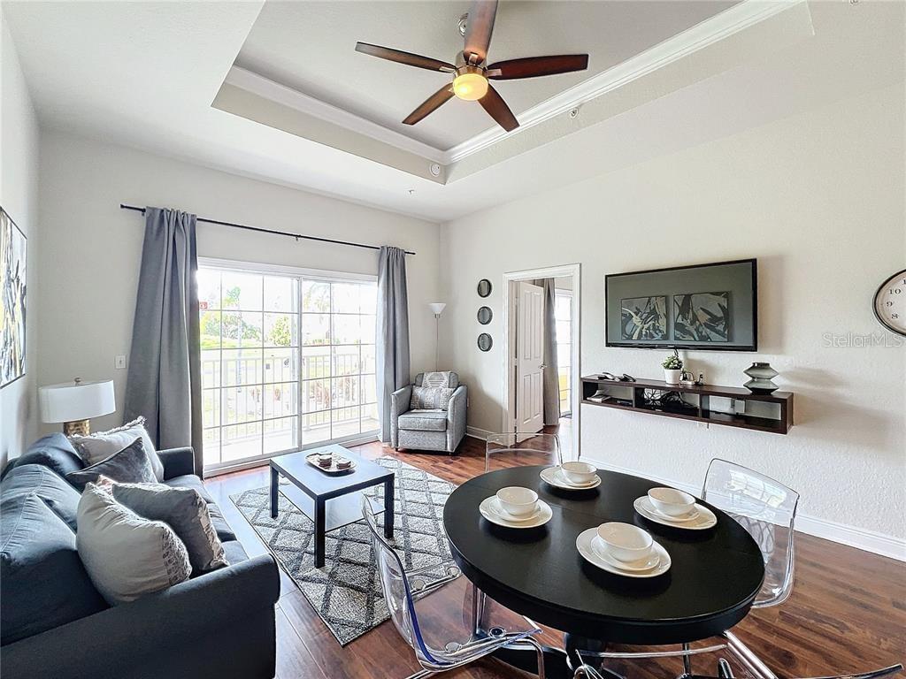 A living and dining area features a tray ceiling, sliding glass doors, and dark wood flooring — 1328 SEVEN EAGLES COURT, REUNION, FL