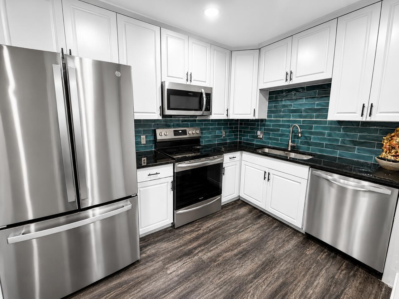 A kitchen with white cabinets, stainless steel appliances, black countertops, and a teal tiled backsplash — 1541 N 14th Terrace, Hollywood FL 33020, HOLLYWOOD, FL