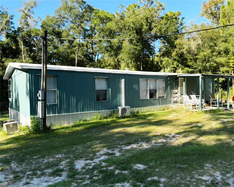 A teal mobile home with a metal roof sits on a grassy lot with trees — 14207 CAROLINA DOVE ROAD, WEEKI WACHEE, FL