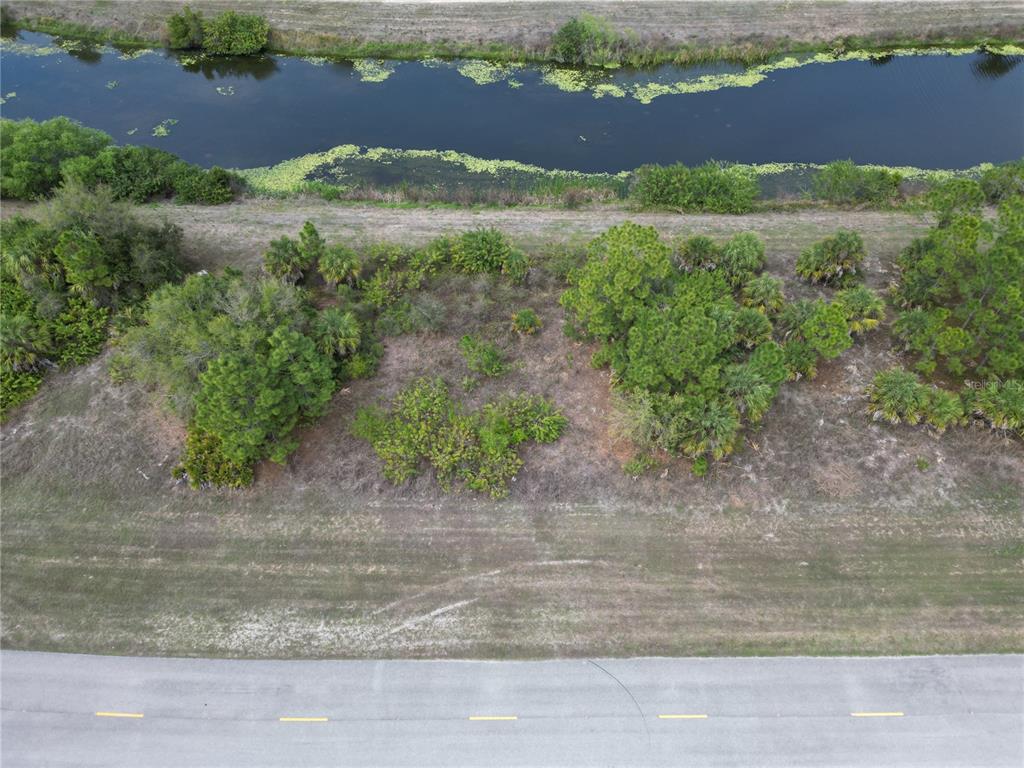 An aerial view shows a vacant, wooded lot situated between a paved road and a canal — S RAINTREE BOULEVARD, NORTH PORT, FL