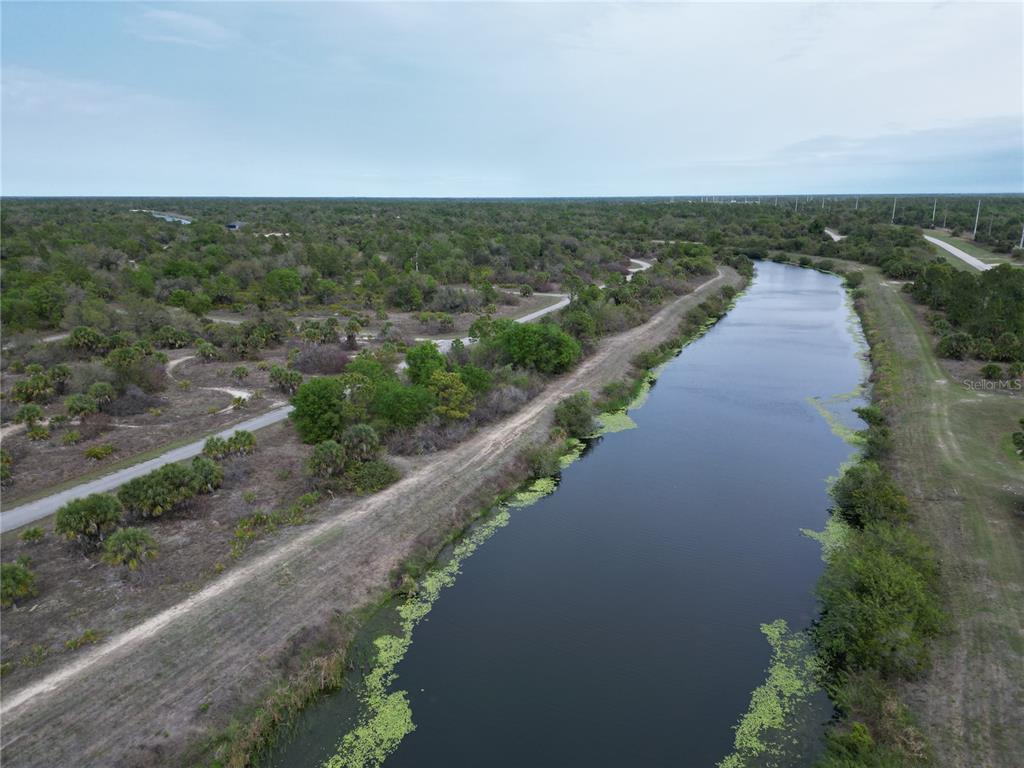 An aerial view shows a long canal running through a wooded landscape with walking paths — S RAINTREE BOULEVARD, NORTH PORT, FL