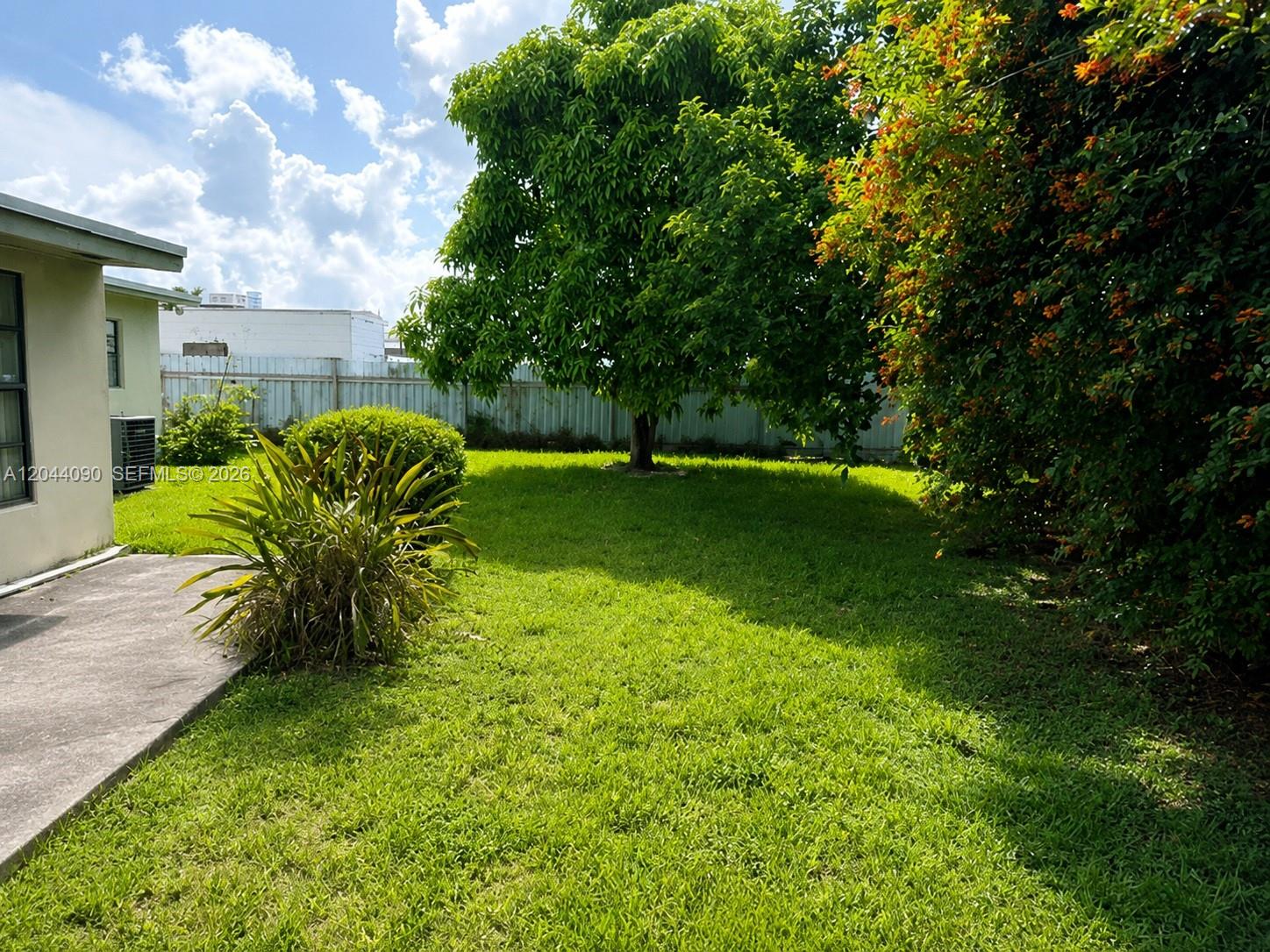 A grassy backyard features a large tree, a flowering hedge, and a concrete patio area — 11832 SW 185th Ter, Miami FL 33177, MIAMI, FL