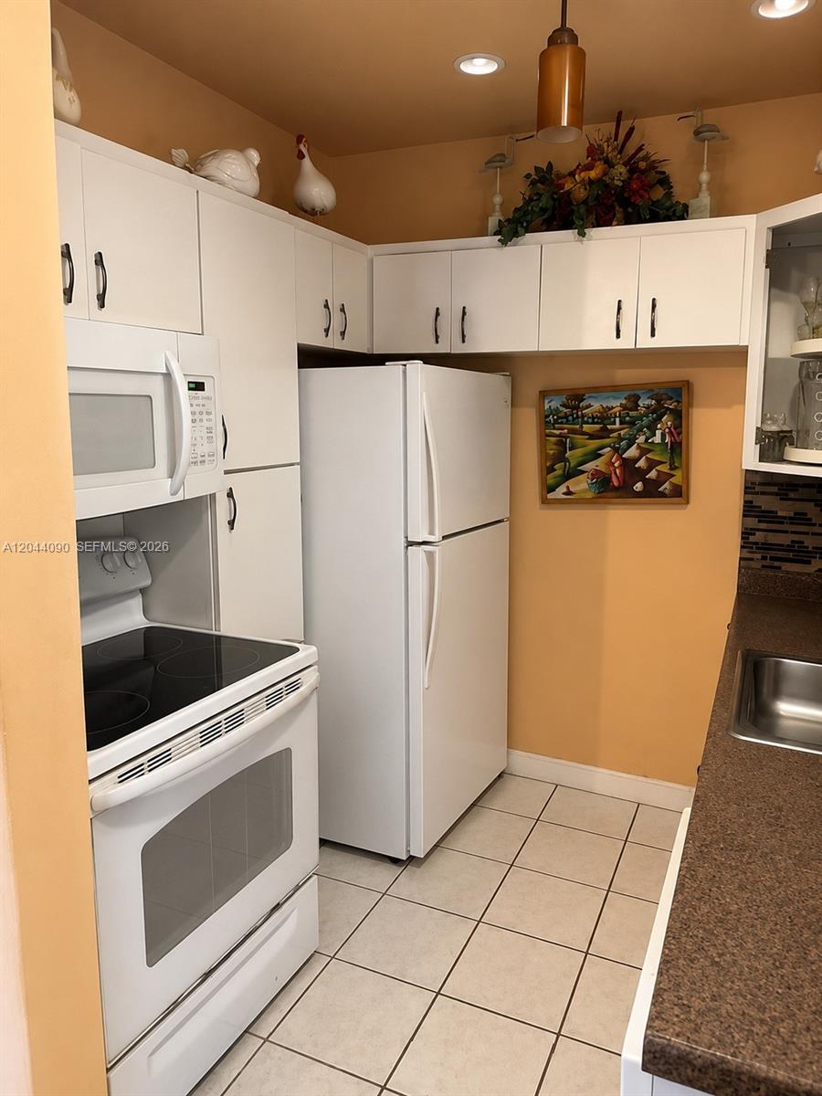 A kitchen features white appliances, white cabinetry, tan walls, and a brown countertop — 11832 SW 185th Ter, Miami FL 33177, MIAMI, FL