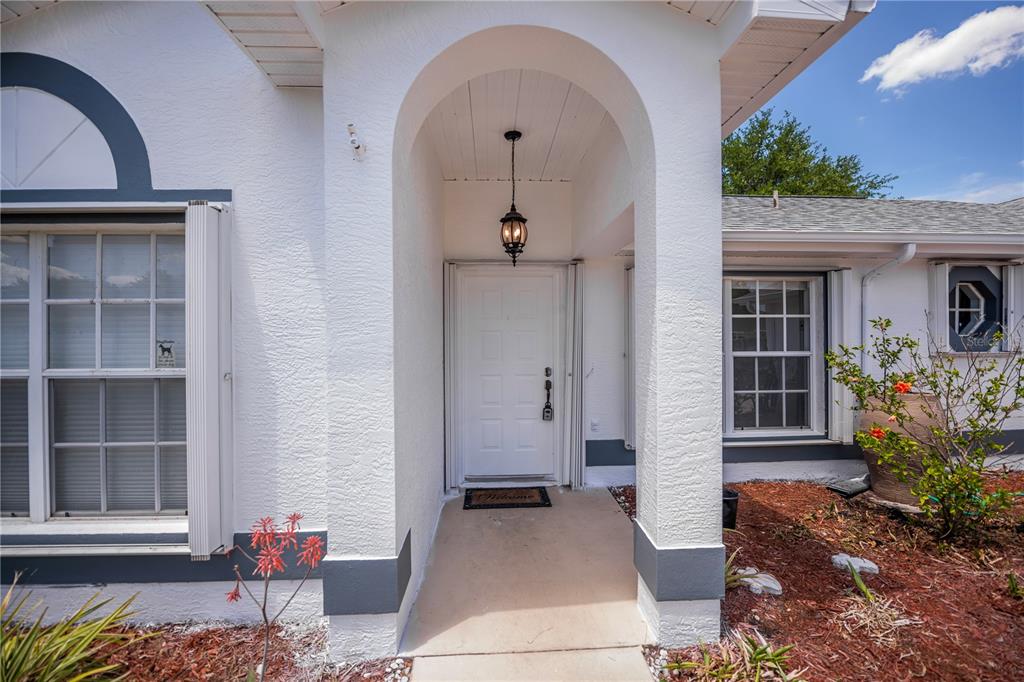 A white front door is recessed within a covered arched entryway of a stucco home — 2618 8TH STREET W, LEHIGH ACRES, FL