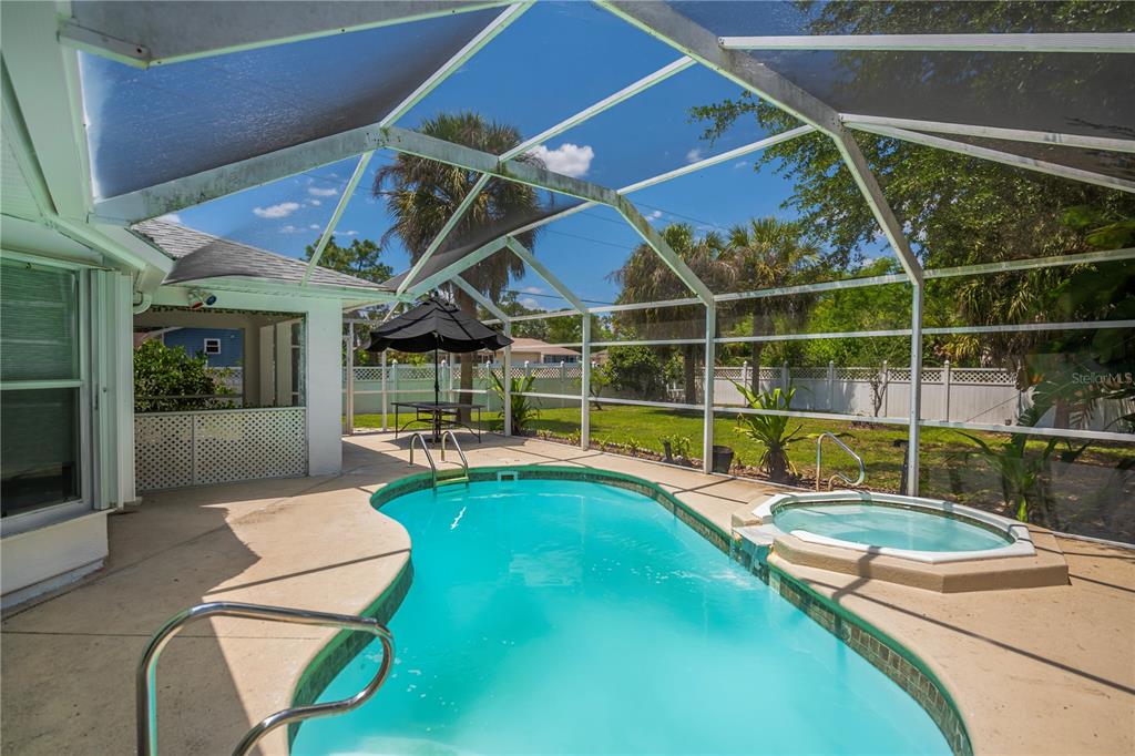 A screened-in patio features a swimming pool, a raised hot tub, and a backyard view — 2618 8TH STREET W, LEHIGH ACRES, FL