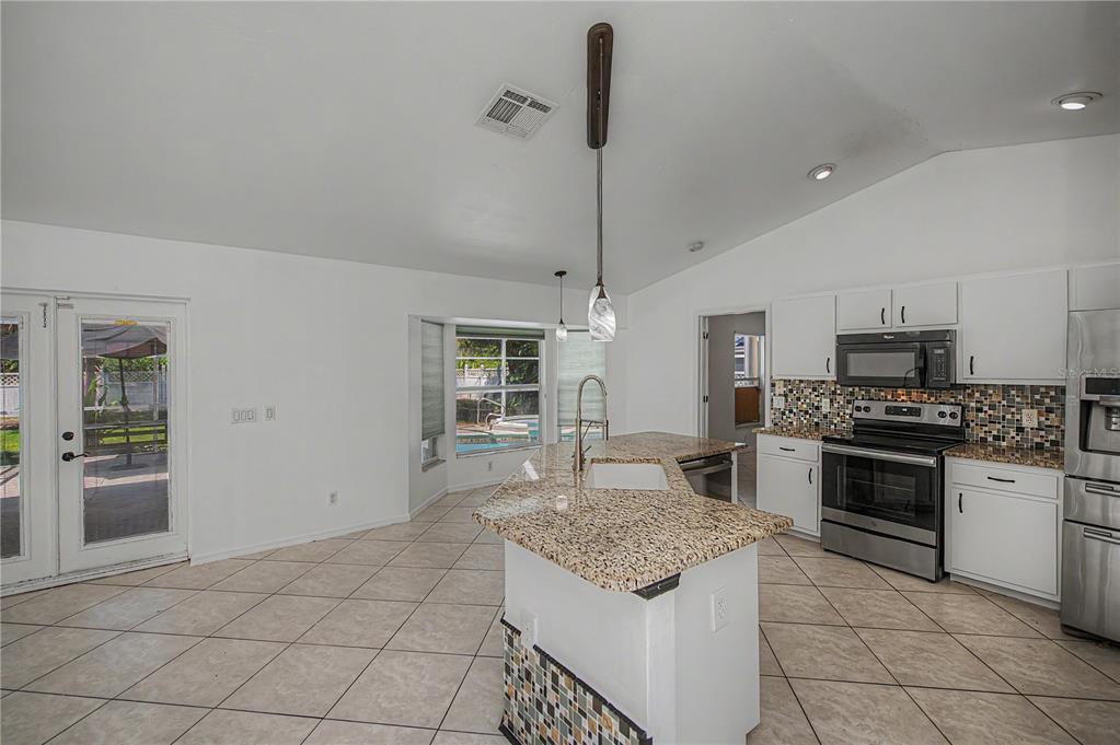 A kitchen features white cabinets, granite countertops, a mosaic backsplash, and a central island — 2618 8TH STREET W, LEHIGH ACRES, FL