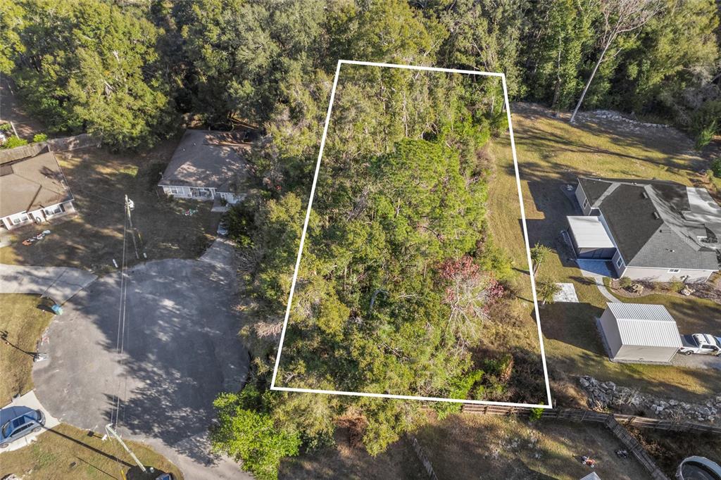 An aerial view shows a wooded, trapezoidal vacant lot outlined in white between two houses — 00 NW 236TH WAY, HIGH SPRINGS, FL