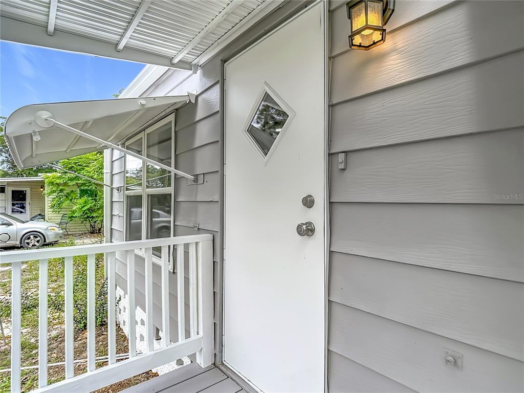 A white door with a diamond-shaped window sits on a porch with gray siding — 12331 PARKWOOD STREET, HUDSON, FL