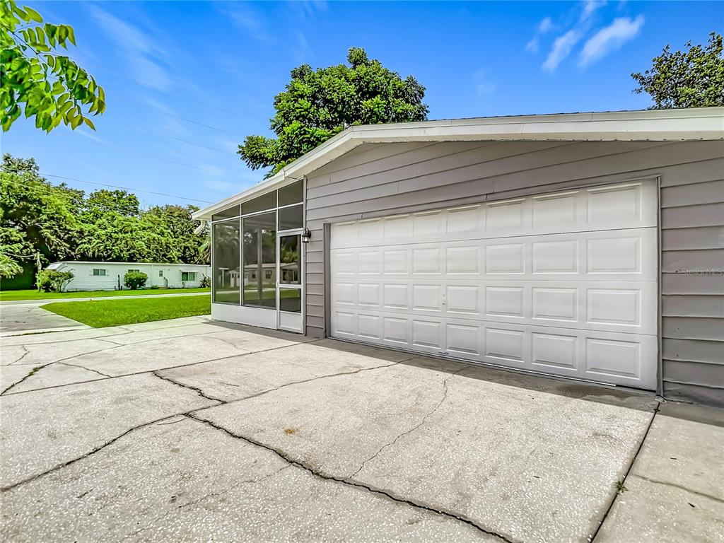 A gray house exterior features a white garage door and an attached screened-in porch — 12331 PARKWOOD STREET, HUDSON, FL