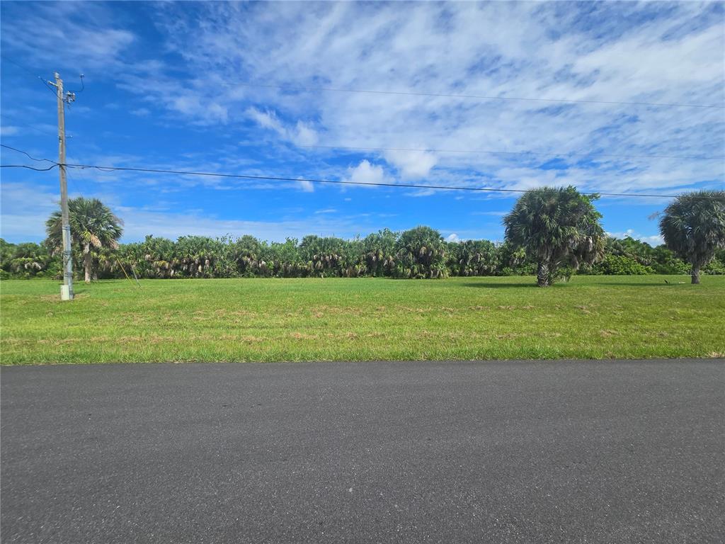 A vacant, grassy lot sits alongside a paved road under a blue, cloudy sky — 16947 ACAPULCO ROAD, PUNTA GORDA, FL
