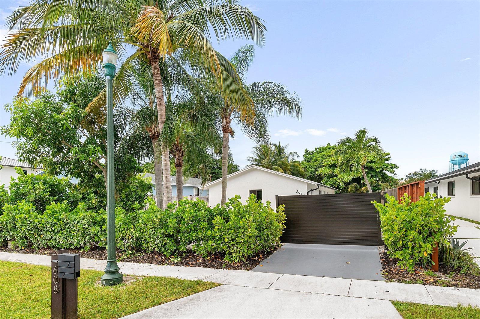 A white house with a dark horizontal gate is partially obscured by palm trees and hedges — 608 SE 2nd Avenue, Delray Beach FL 33483, DELRAY BEACH, FL