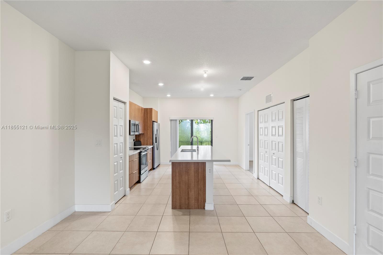 A modern kitchen features wood-toned cabinetry, a central island with a sink, and tile flooring — 7831 NW 104th Ave # 22, Doral FL 33178, DORAL, FL