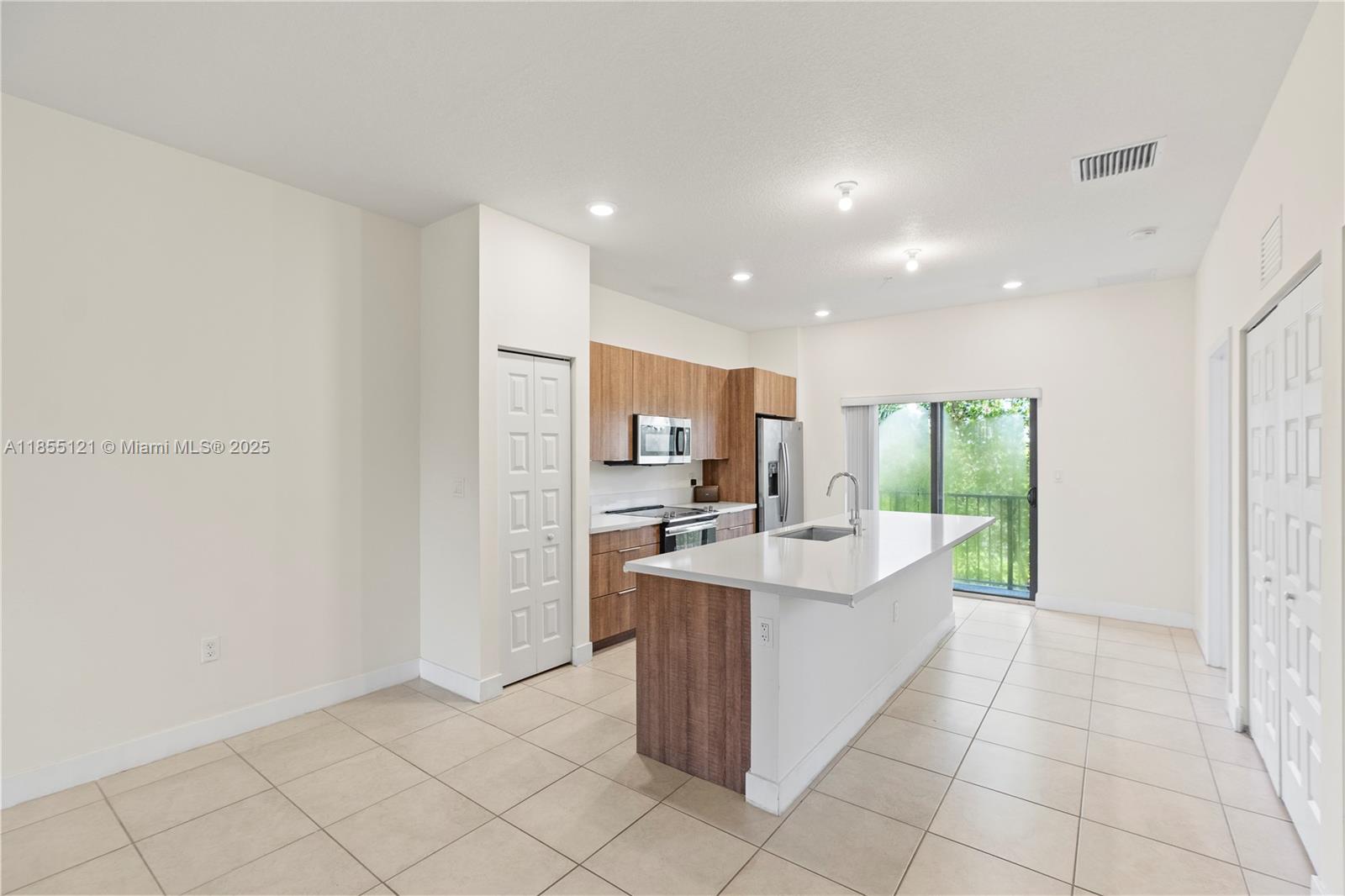 A modern kitchen features wood-tone cabinetry, a white island, and tile flooring — 7831 NW 104th Ave # 22, Doral FL 33178, DORAL, FL