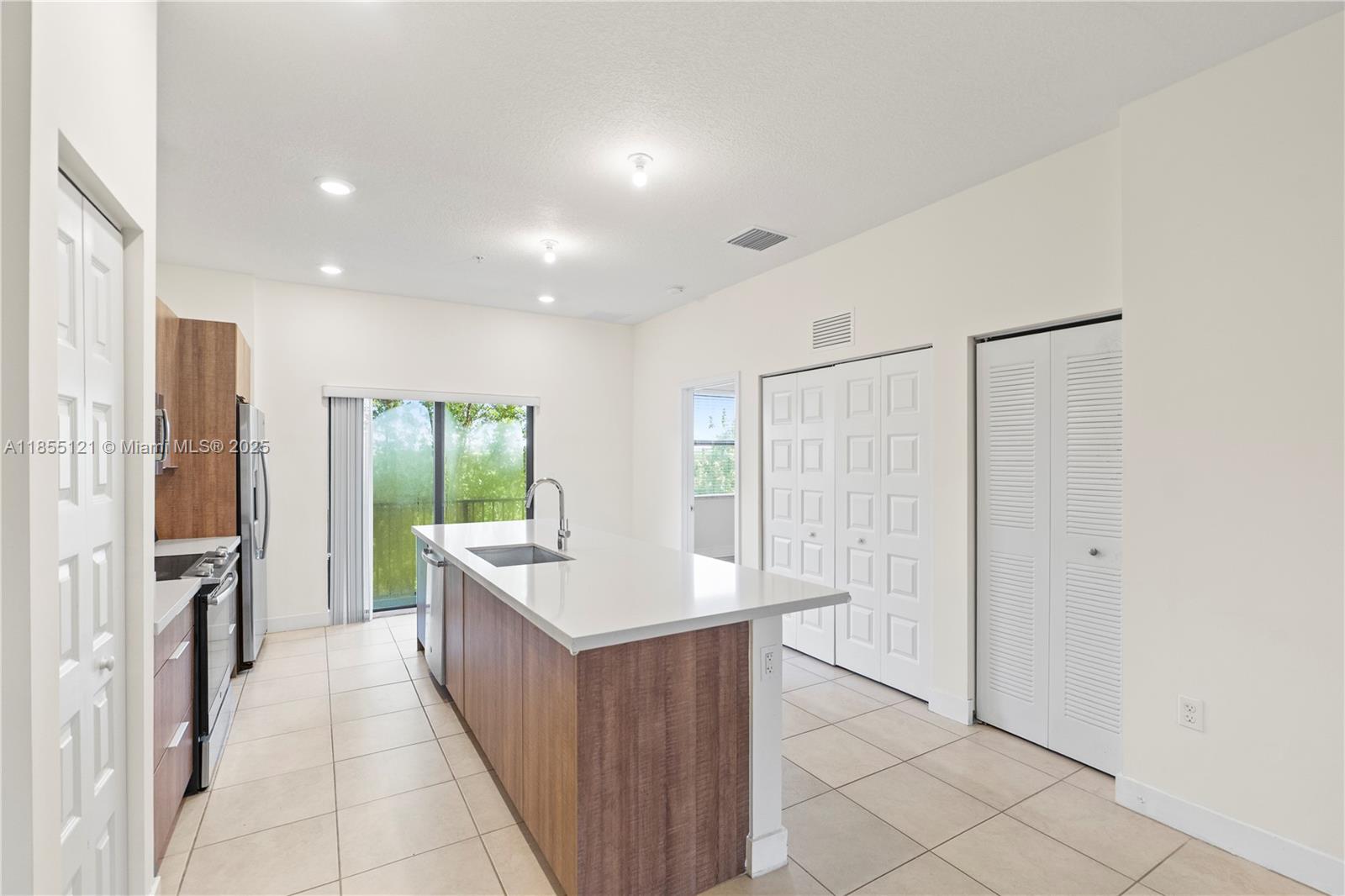 A kitchen features a central island with a sink, light tile flooring, and white cabinetry — 7831 NW 104th Ave # 22, Doral FL 33178, DORAL, FL