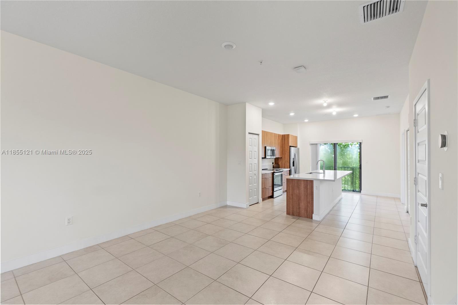 An open-concept kitchen with wood-toned cabinets and a central island overlooks a tiled living area — 7831 NW 104th Ave # 22, Doral FL 33178, DORAL, FL