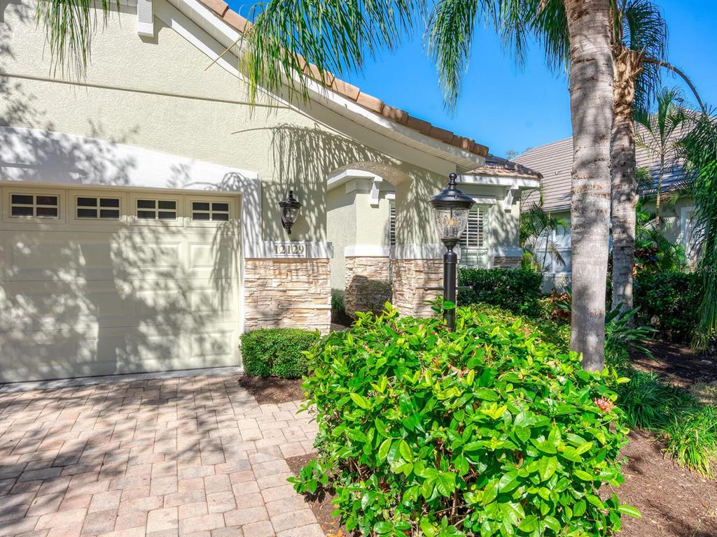 A bright entryway features white walls, light wood flooring, a chandelier, and a glass-paneled door — 12129 THORNHILL COURT, LAKEWOOD RANCH, FL