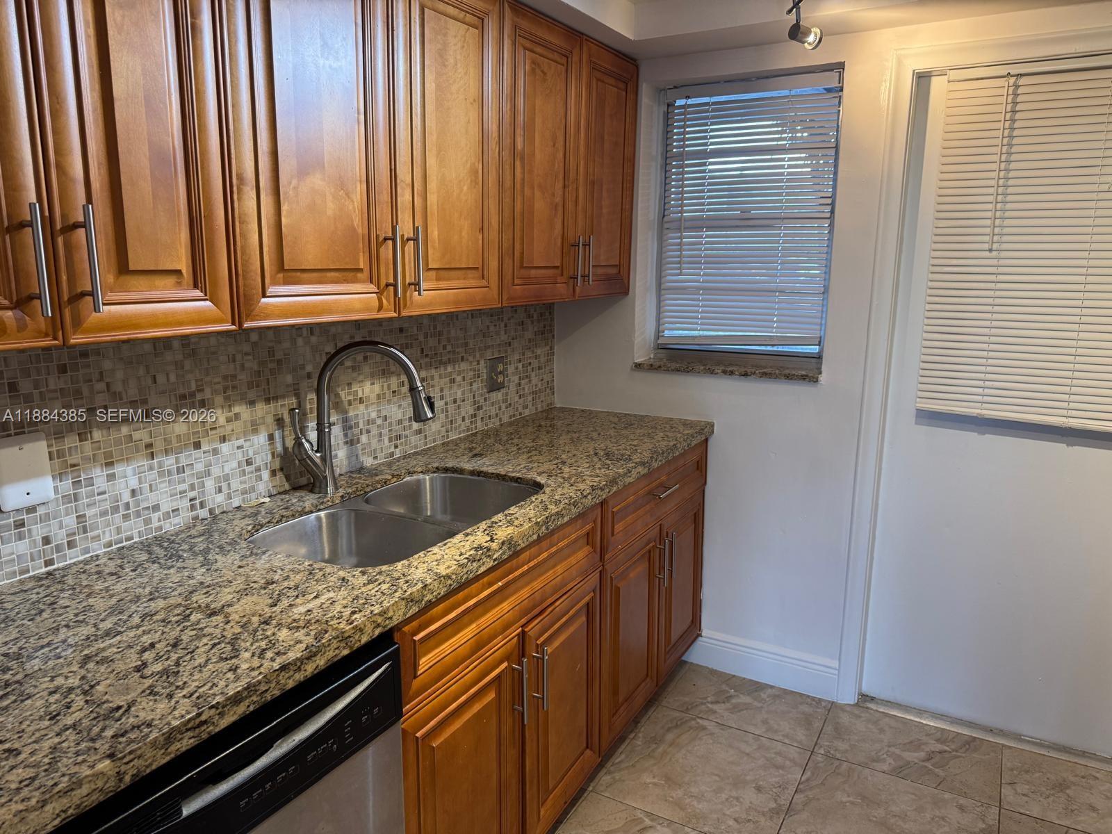 A kitchen features wood cabinets, granite countertops, a stainless steel sink, and a tiled backsplash — 2471 SW 82nd Ave # 108, Davie FL 33324, DAVIE, FL