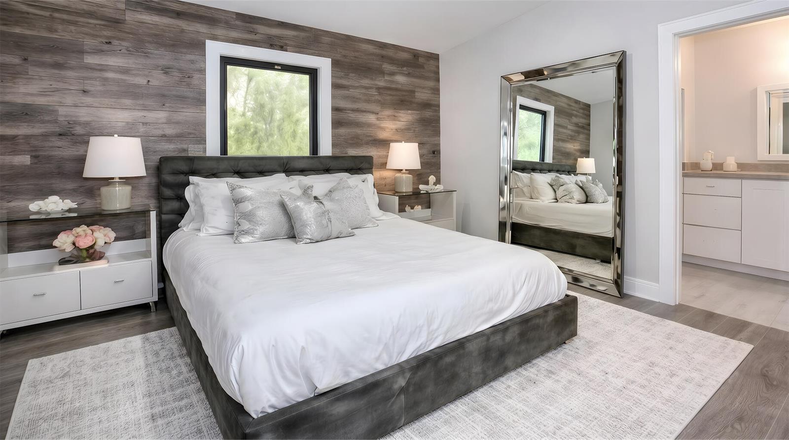 A bedroom features a tufted bed, wood-plank accent wall, large floor mirror, and attached bathroom — 2112 NW 83rd Street, Miami FL 33147, MIAMI, FL