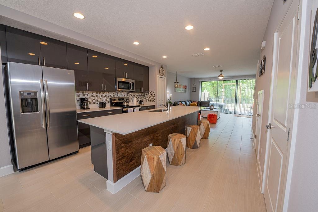 A modern kitchen features dark gray cabinets, a white island with wood paneling, and stools — 4730 TERRA ESMERALDA DRIVE, KISSIMMEE, FL