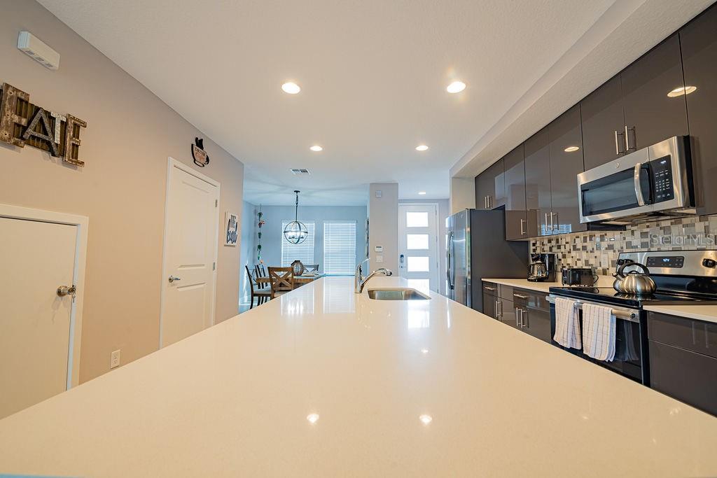 A modern kitchen features a long white quartz island, gray cabinets, and stainless steel appliances — 4730 TERRA ESMERALDA DRIVE, KISSIMMEE, FL