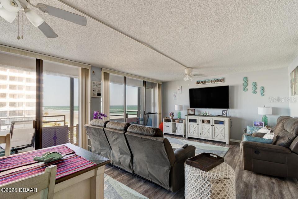A living room features a large television, brown reclining furniture, and sliding glass doors overlooking the ocean — 2828 N ATLANTIC AVENUE UNIT 303, DAYTONA BEACH, FL