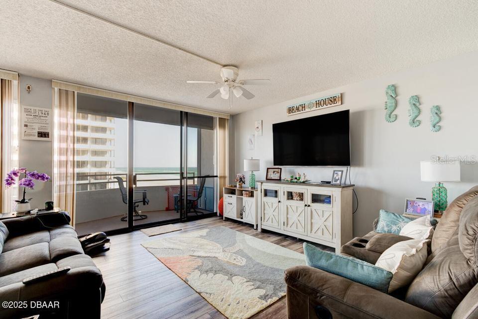 A living room features a television, a white media console, and a balcony with ocean views — 2828 N ATLANTIC AVENUE UNIT 303, DAYTONA BEACH, FL