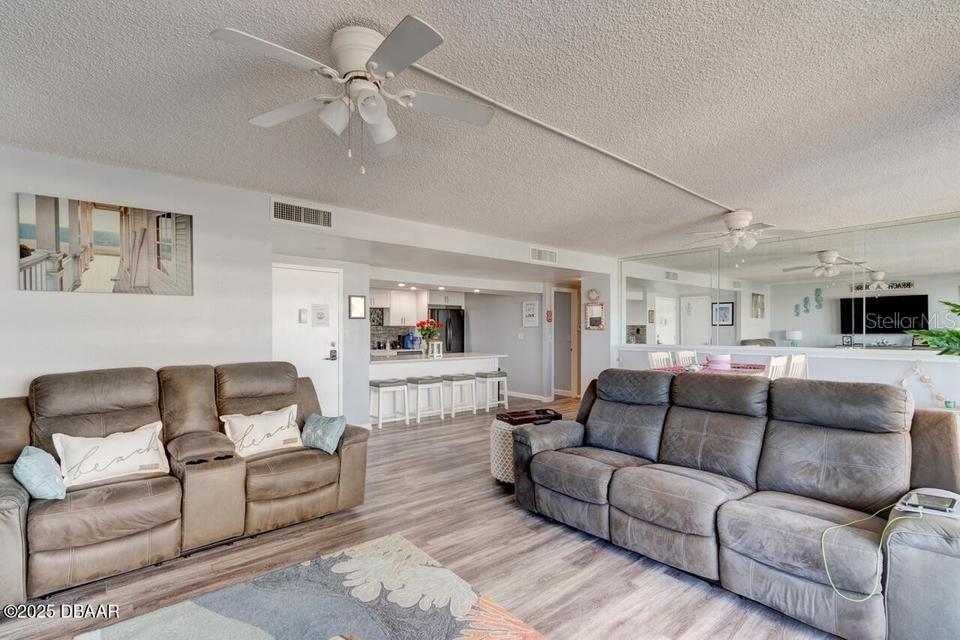 A living room with two grey sofas, light wood flooring, and an open kitchen area — 2828 N ATLANTIC AVENUE UNIT 303, DAYTONA BEACH, FL