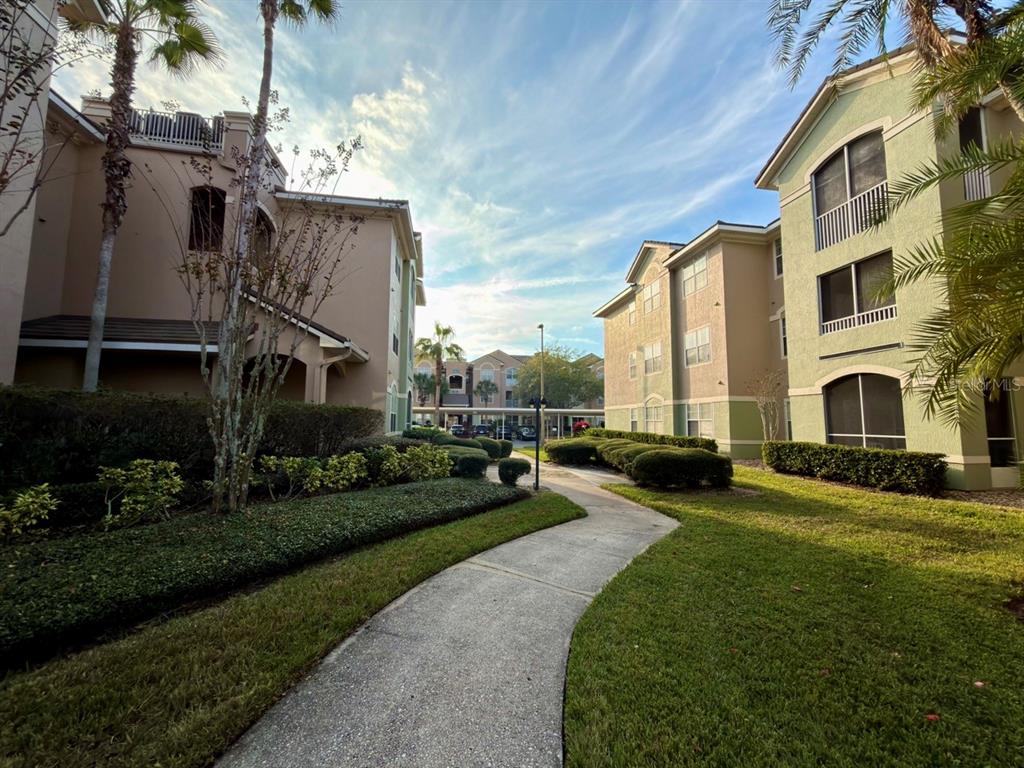 A paved walkway leads between two multi-story apartment buildings surrounded by landscaped lawns and palm trees — 4865 CYPRESS WOODS DRIVE UNIT 2302, ORLANDO, FL