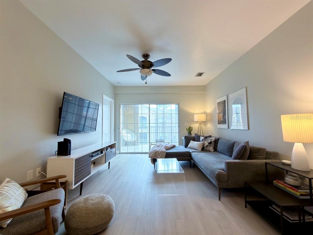 A living room features light wood flooring, a gray sectional sofa, and a sliding glass door — 4865 CYPRESS WOODS DRIVE UNIT 2302, ORLANDO, FL