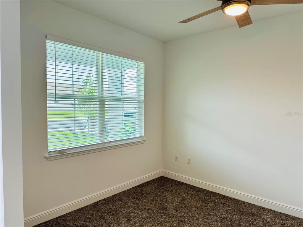 A bedroom with white walls, dark carpeting, a ceiling fan, and a large window — 5806 SW 78TH AVENUE ROAD, OCALA, FL